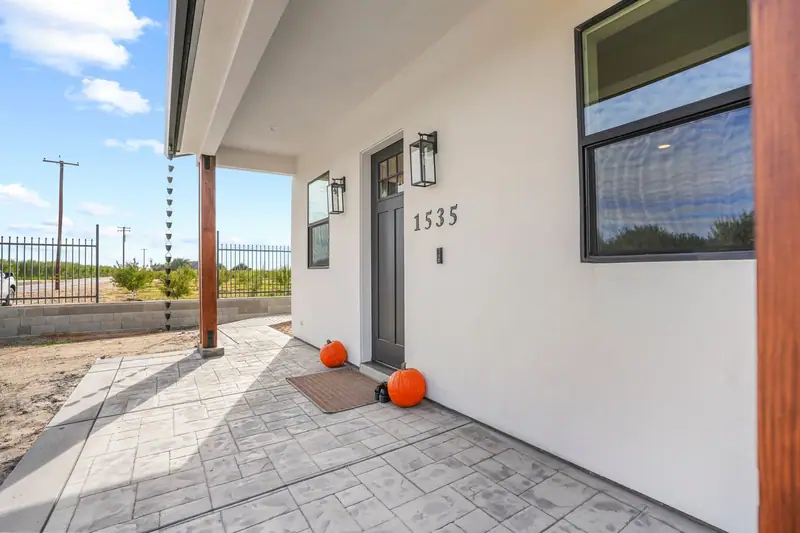 Covered front porch of a newly built white home with stamped concrete and pumpkins by the door
