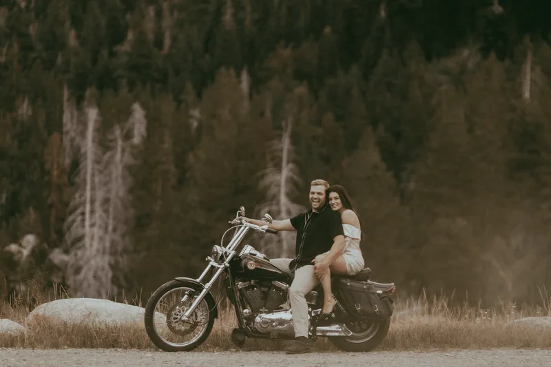 Couple sitting on a motorcycle in front of a pine forest